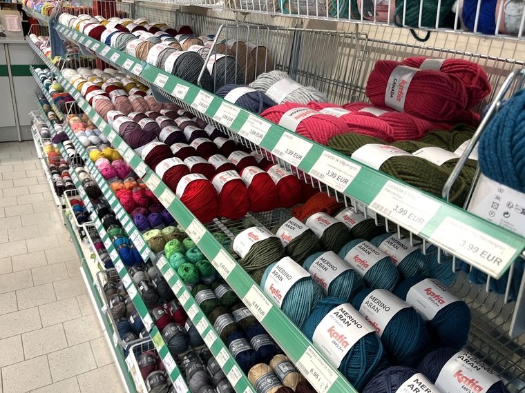 Regal mit farblich sortierten Wollknäueln verschiedener Marken und Preisschildern